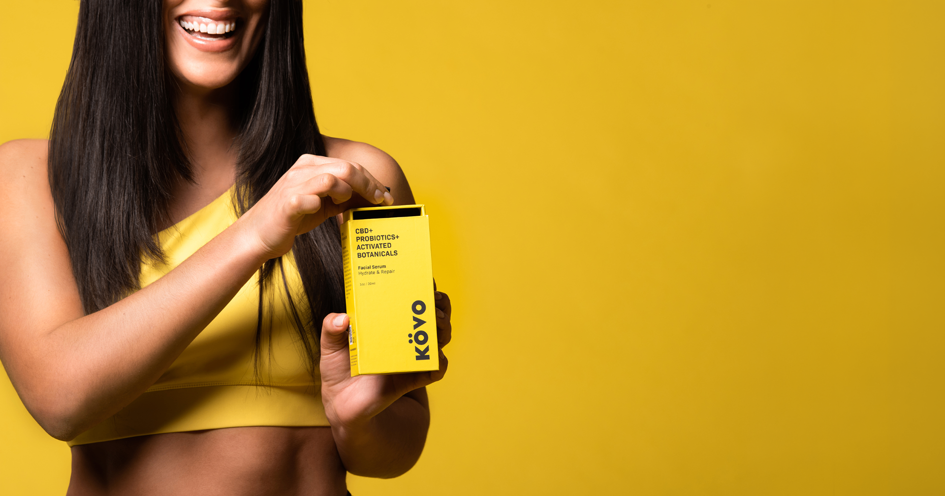 Smiling Kovo founder holding the yellow CBD facial serum packaging